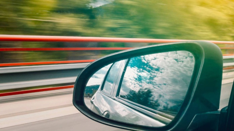 Car left side mirror with sky and trees reflecting in it